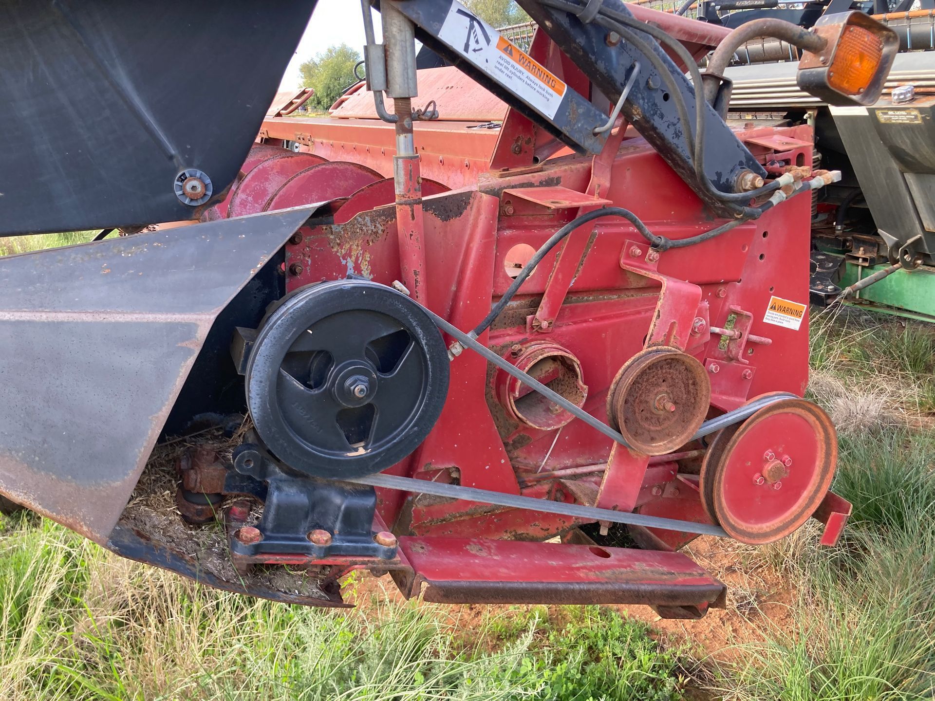 Red tractor-mounted rotary mower with black belts and red wheels in a grassy field