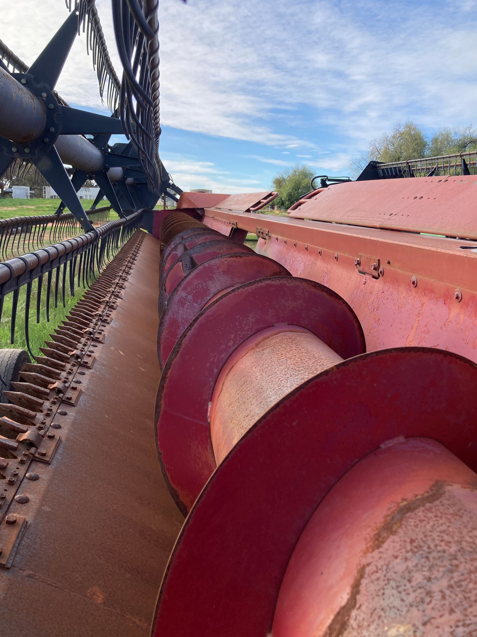 Close-up of red auger machinery on a farm under a blue sky