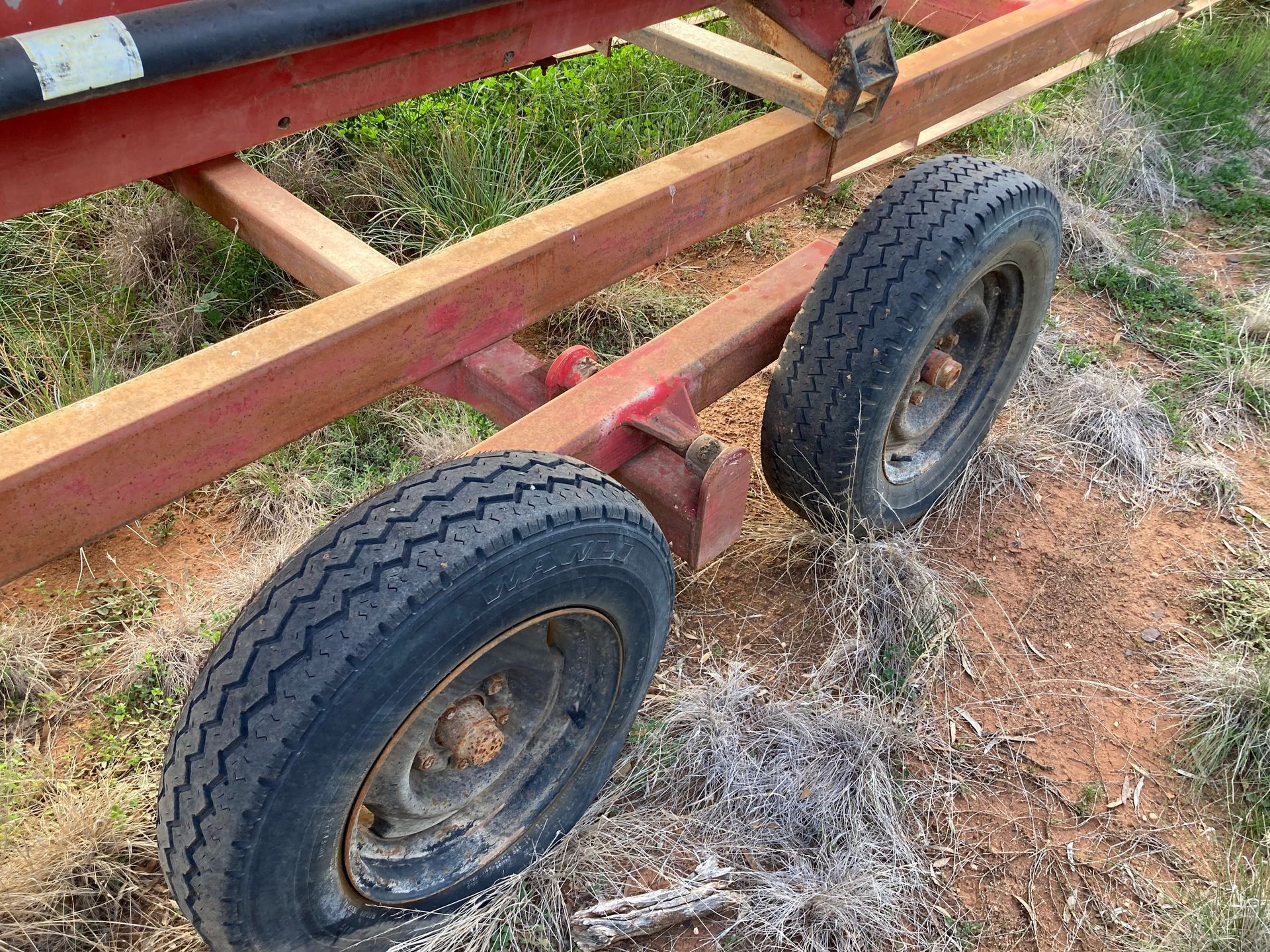 Rusty trailer frame with two black wheels on dirt and grass