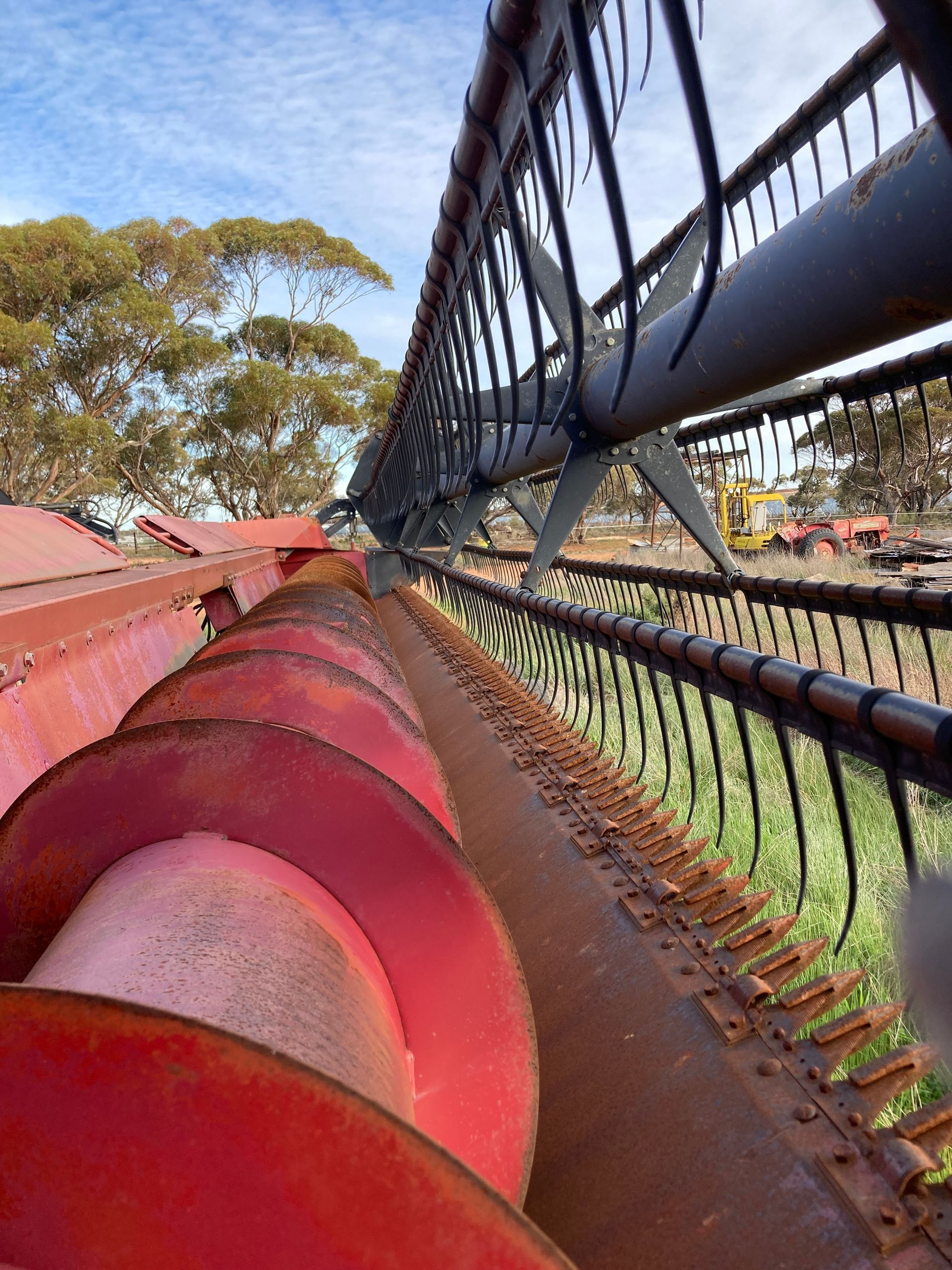 Close-up of red metal wheels along a conveyor beside a wire fence, with trees in the background