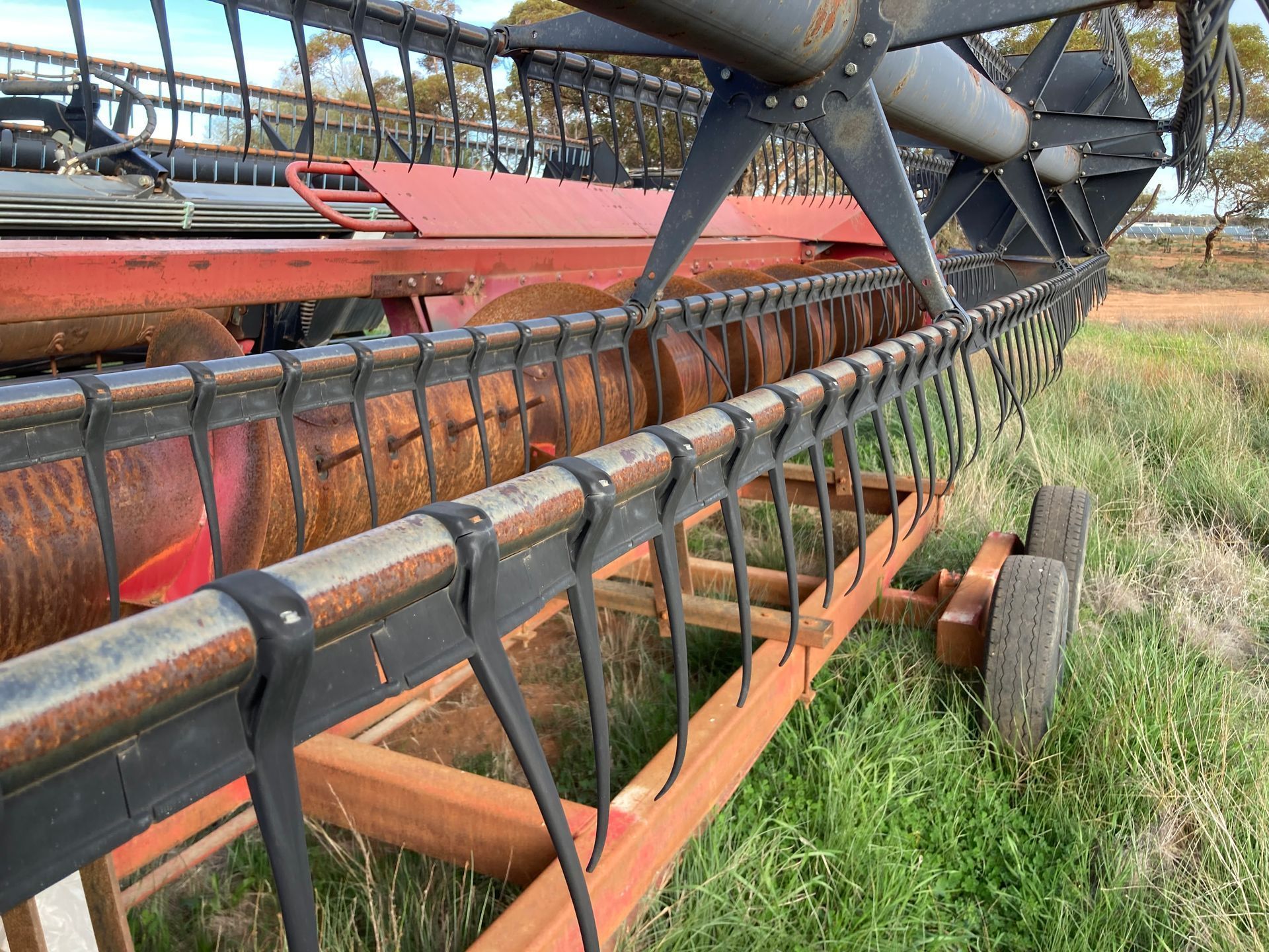 Rusty farm combine header with black reel parked in a grassy field