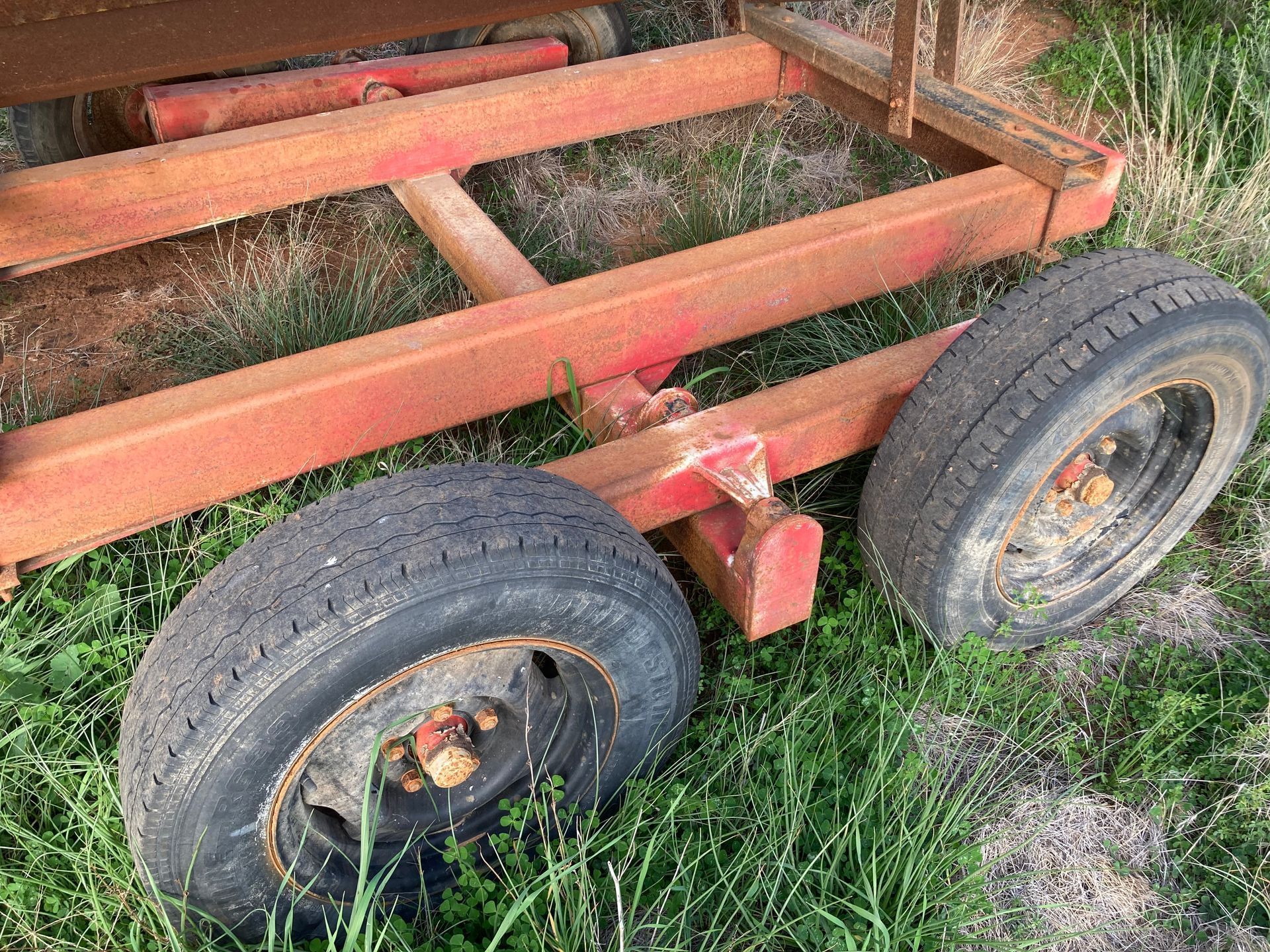 Rusty red trailer frame with two worn tires sitting in grass