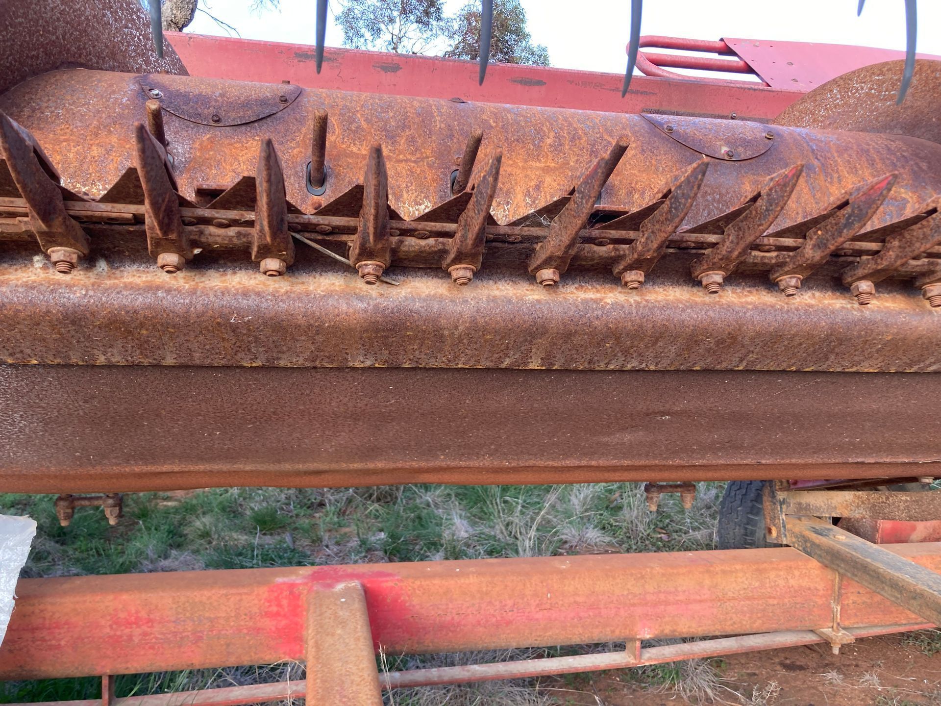 Close-up of rusty metal teeth on orange machinery against an outdoor background