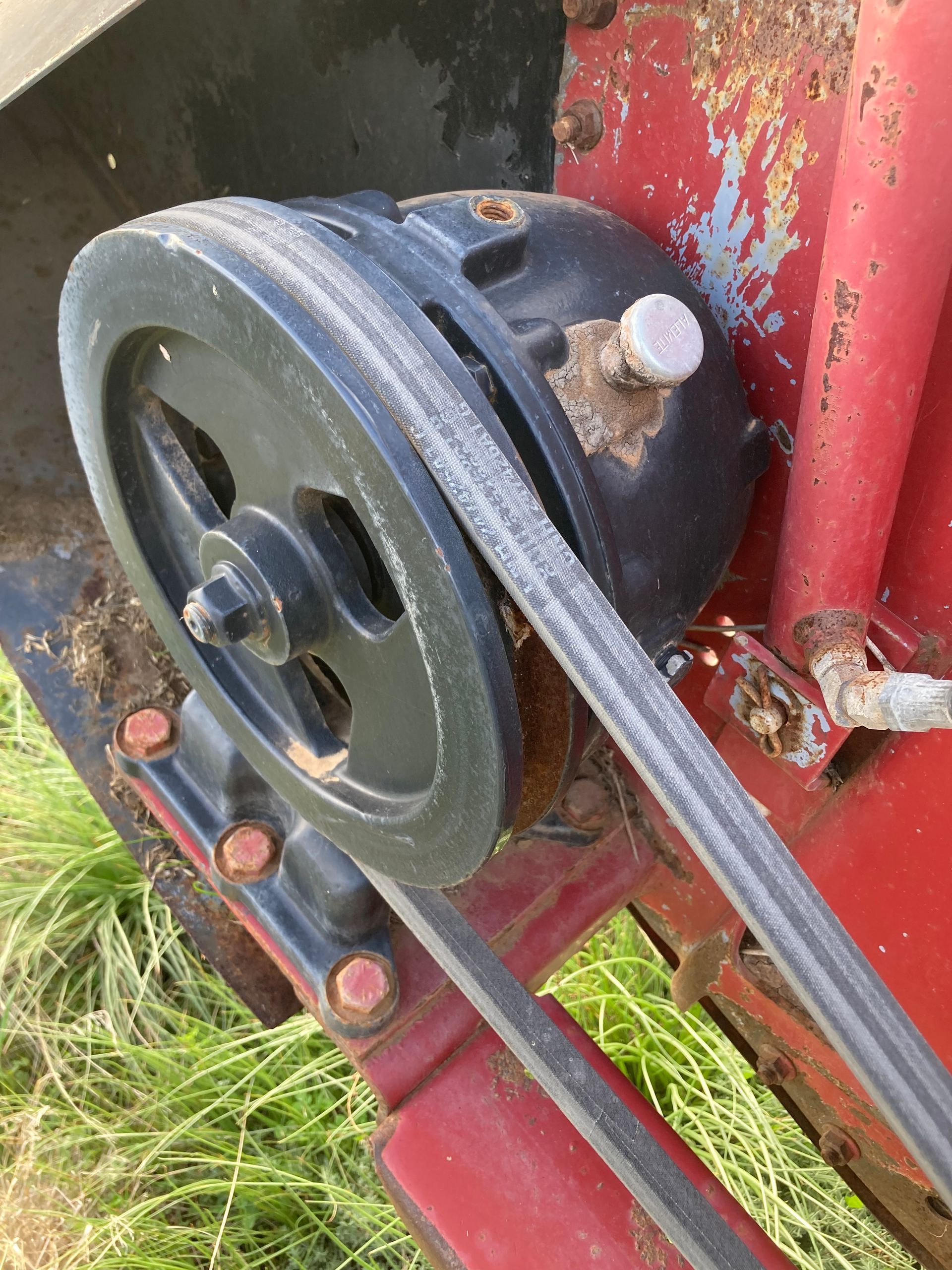 Close-up of a black pulley and belt on a red machine outdoors in grass.