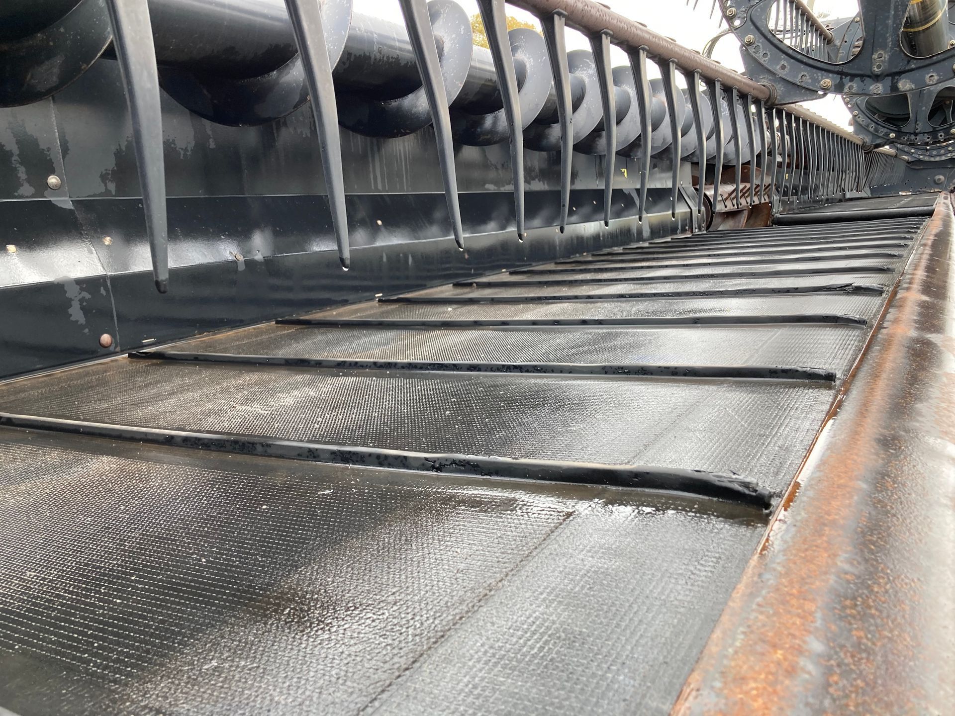 Close-up of a metal conveyor belt carrying dark granular material in an industrial setting.