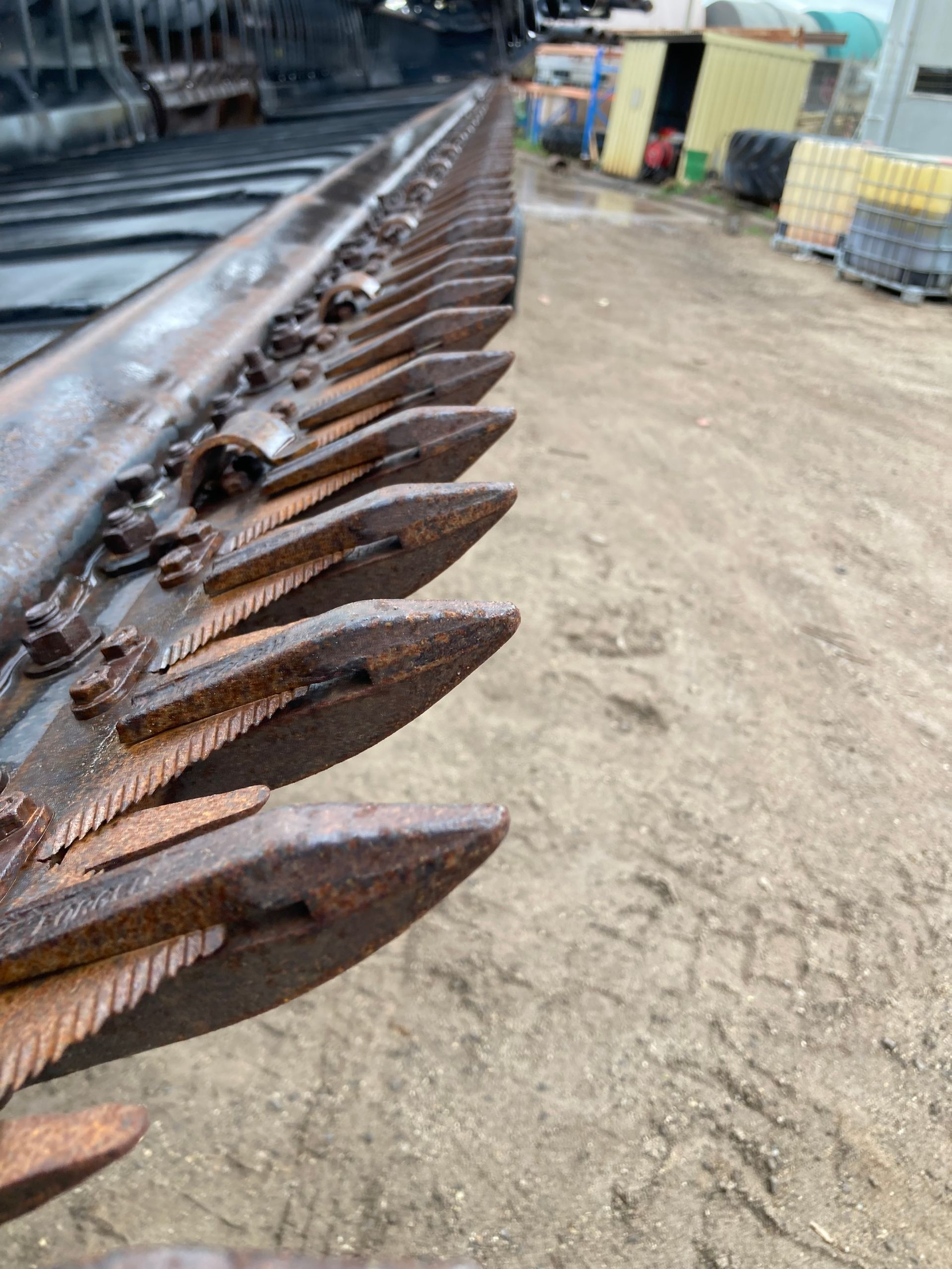 Rows of rusted metal tools or tines lined up on a worksite floor beside machinery