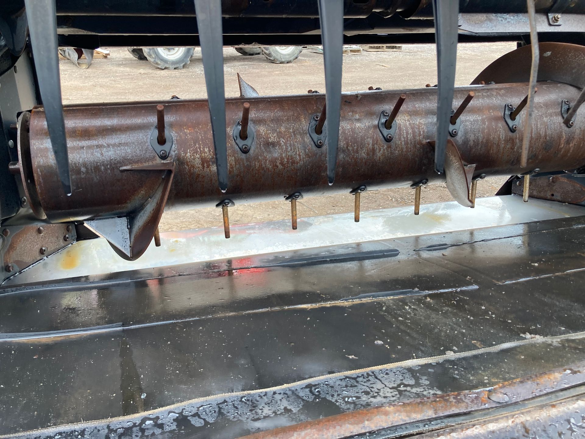 Close-up of a rusty metal auger or conveyor with bolts above a wet concrete floor