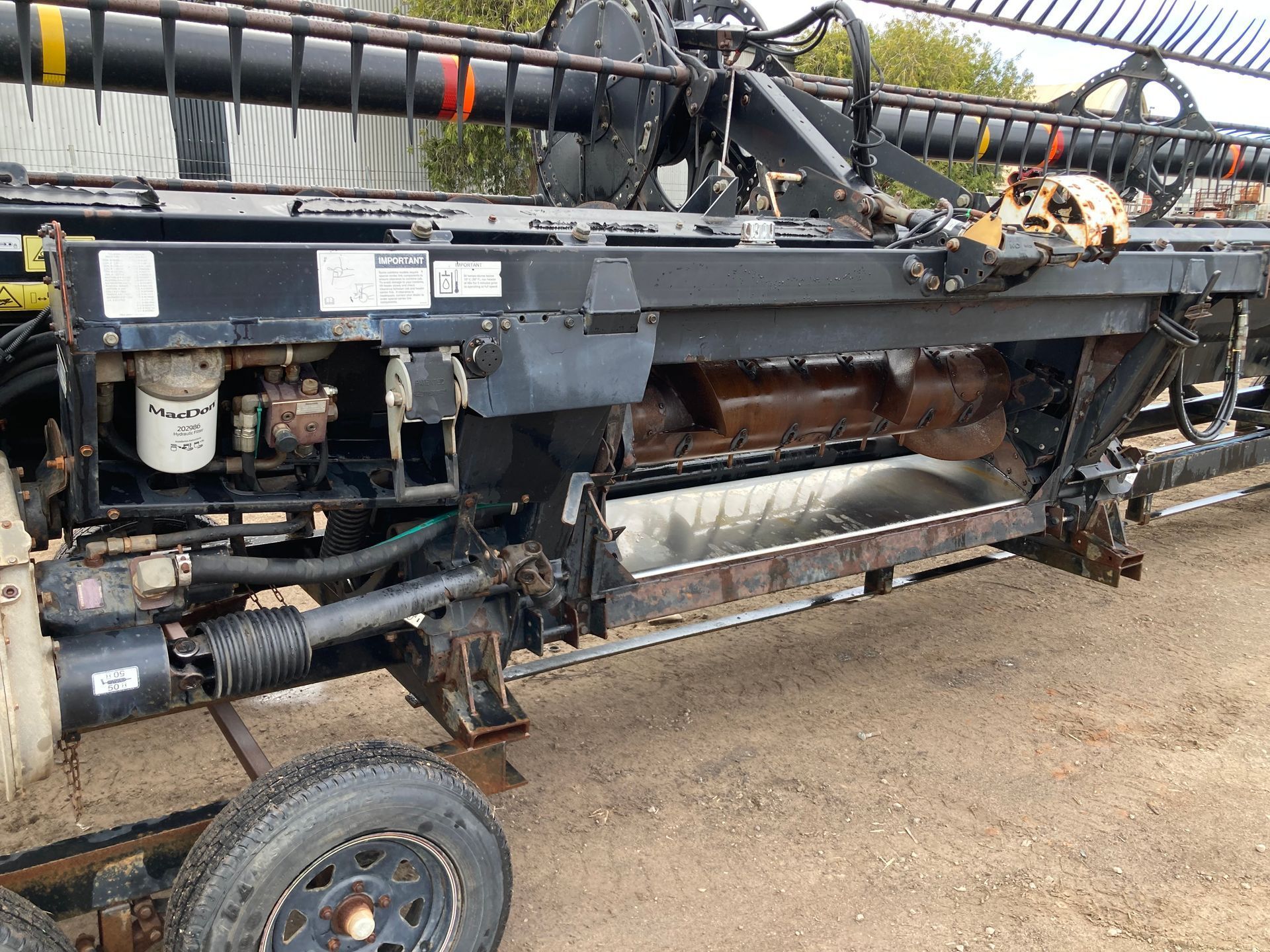A dusty agricultural combine with a large cutting header and exposed machinery, parked outdoors.