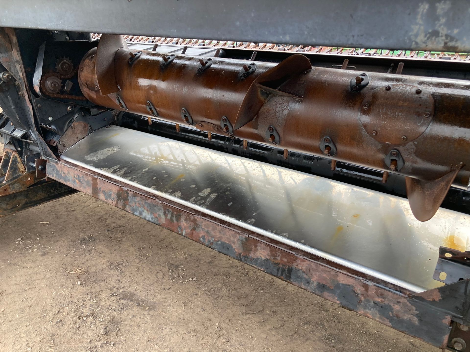Industrial auger conveyor above a metal chute, with debris in a dusty work area