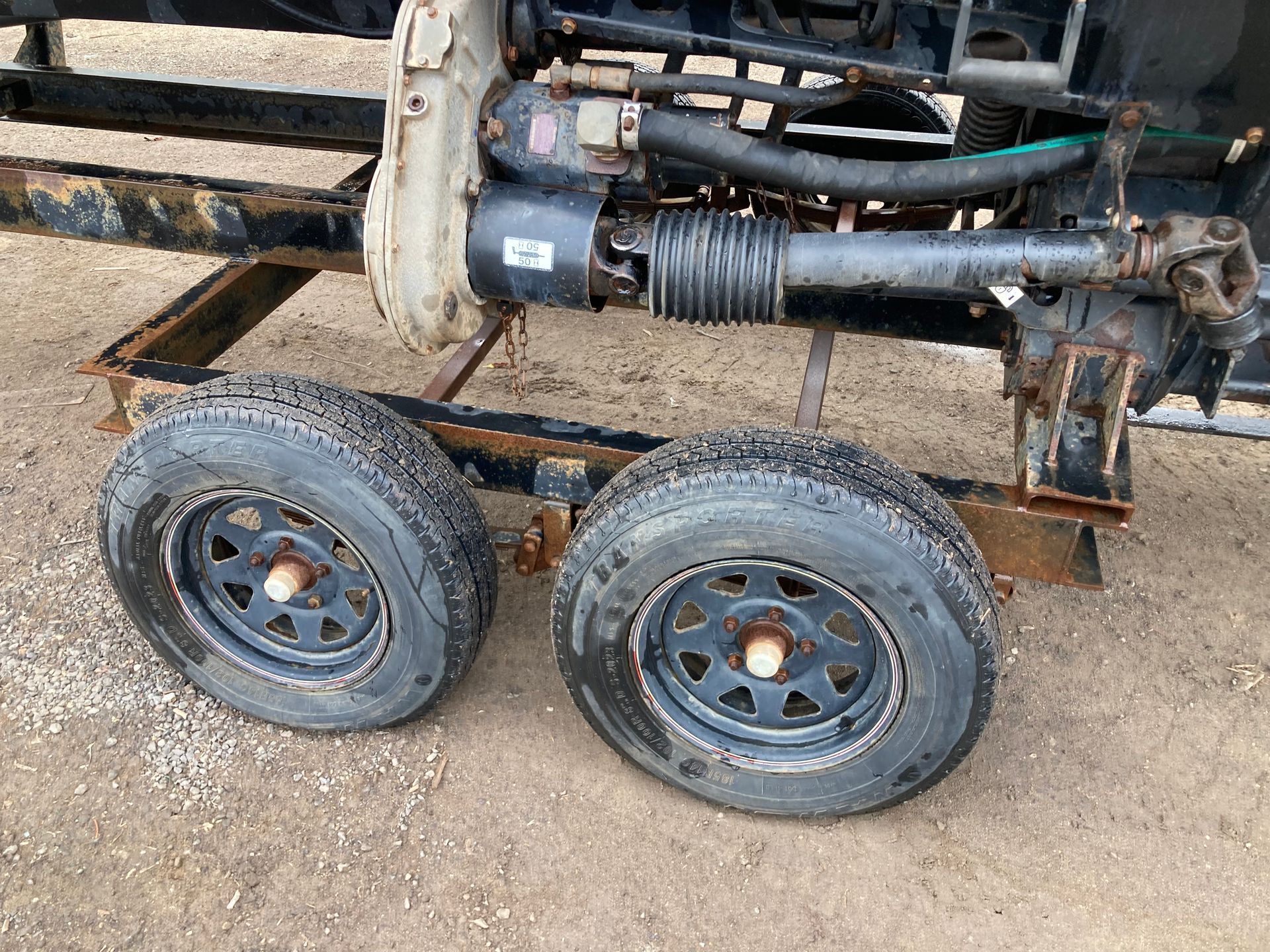 Small two-wheel utility trailer with visible hydraulic components on a gravel surface.