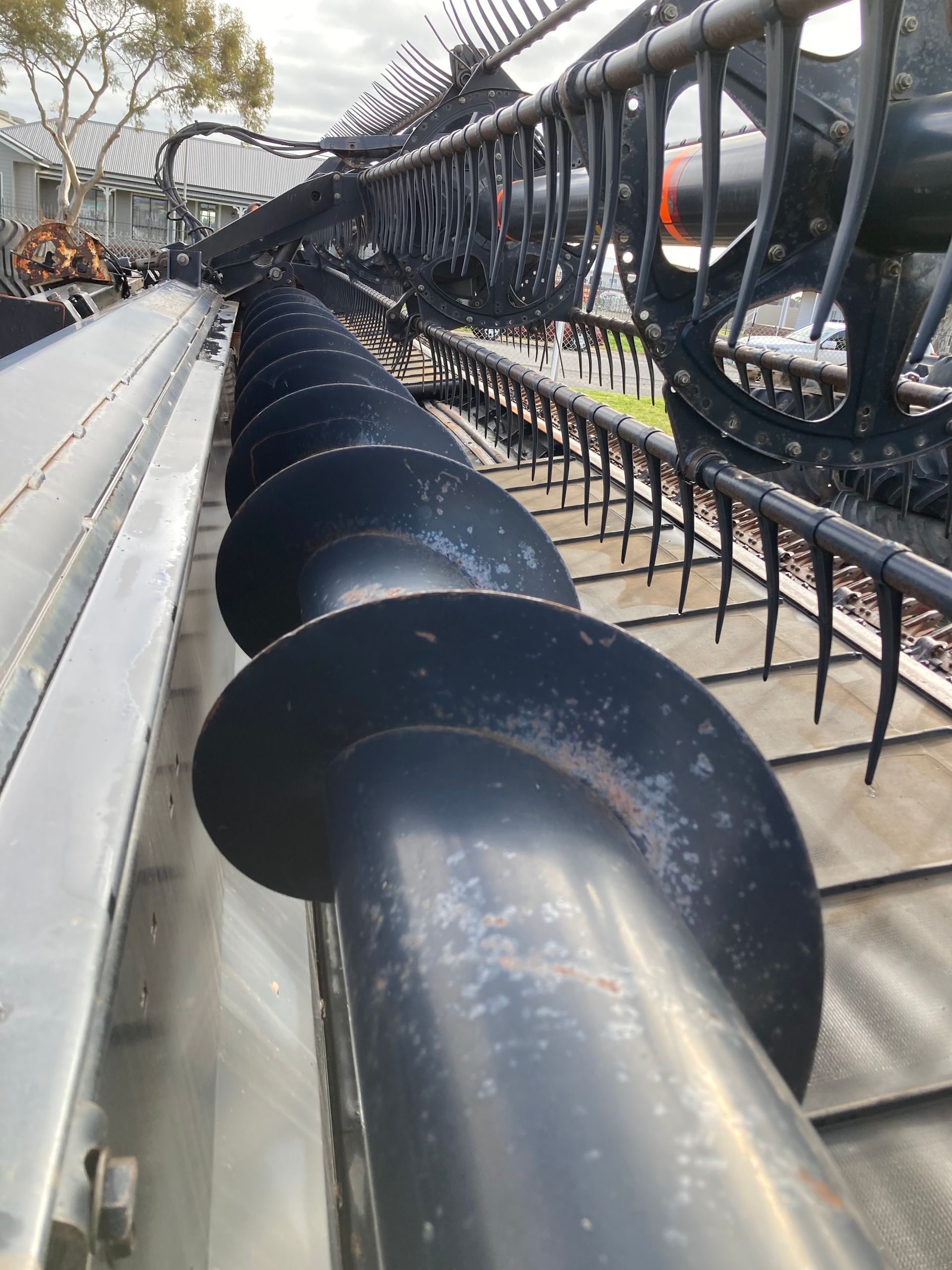Close-up of a black auger conveyor beside a metal frame, outdoors on a worksite.