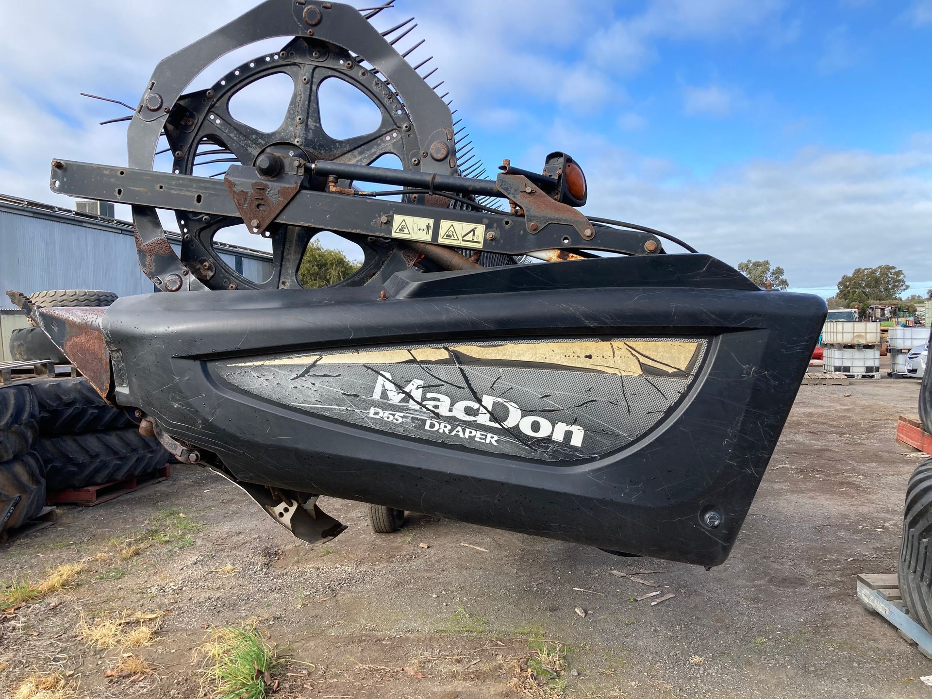 Large black MacDon agricultural header attachment on the ground in an outdoor lot.