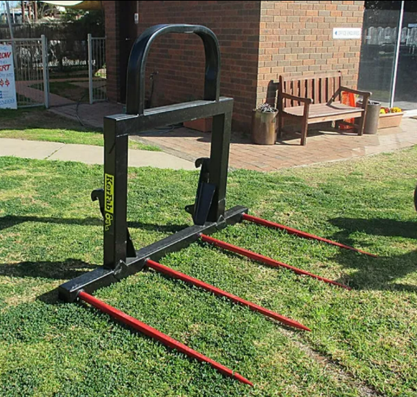 Black agricultural attachment with red tines on grass near a brick building