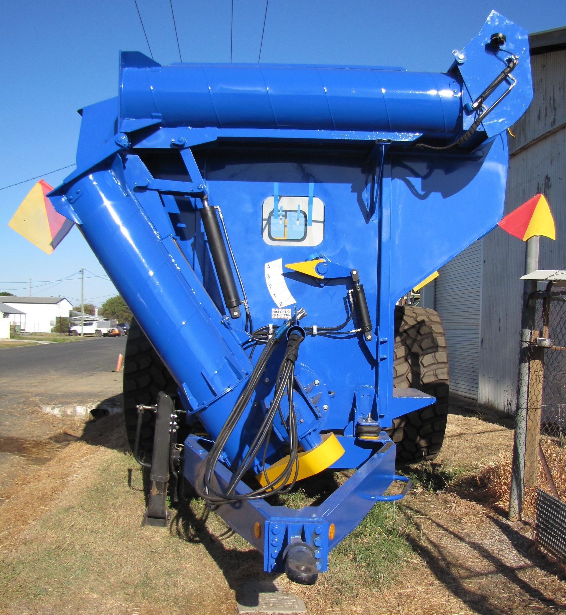 Blue farm machinery with yellow accents parked outdoors beside a building.