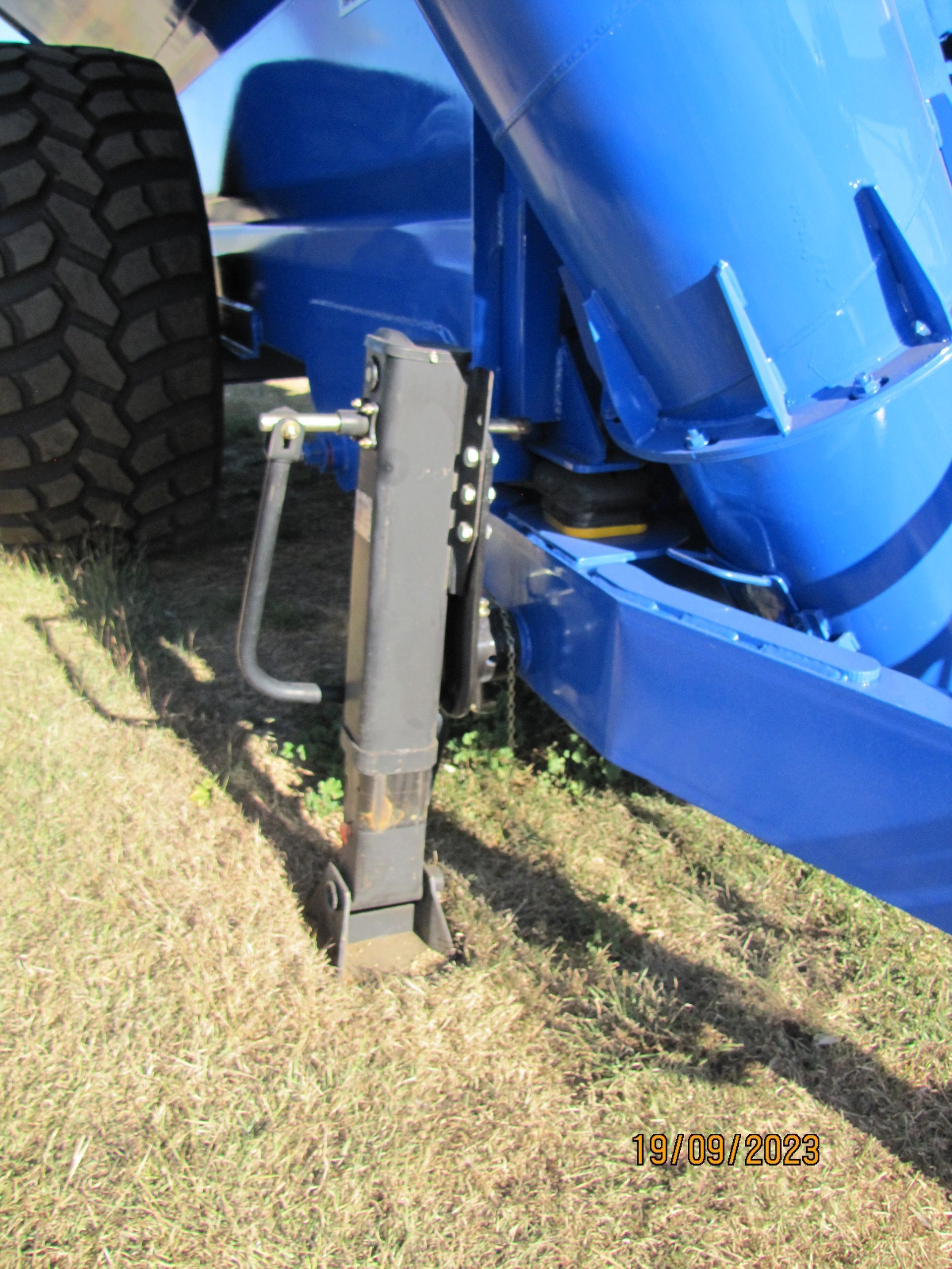 Black hydraulic jack attached to a blue off-road vehicle, lifting it on grass.