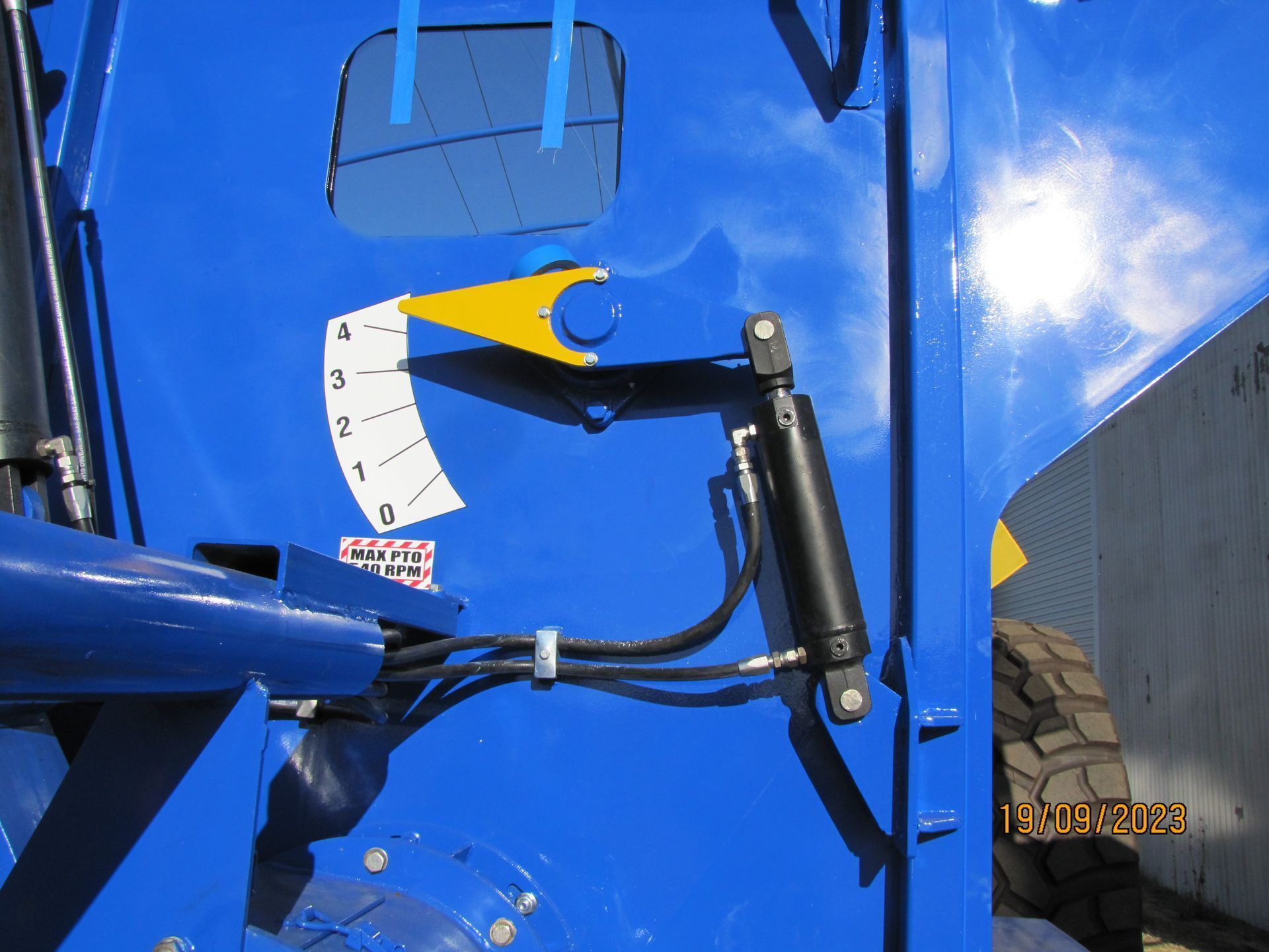 Blue tractor rear hitch mechanism with hydraulic cylinder and wheel visible.