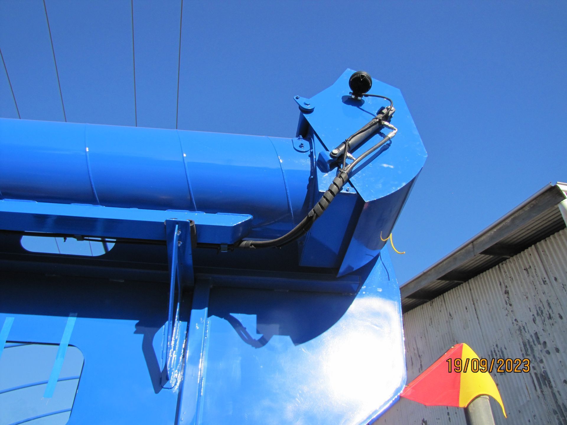 Blue industrial machine with hydraulic hose against a clear blue sky
