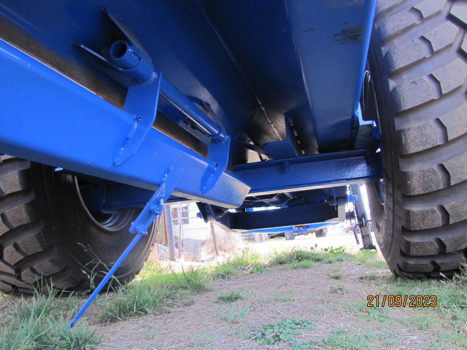 Blue vehicle chassis with large tires seen from underneath on a dirt surface.