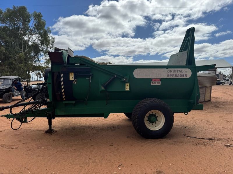 Green agricultural machine on wheels parked on red dirt under a cloudy sky