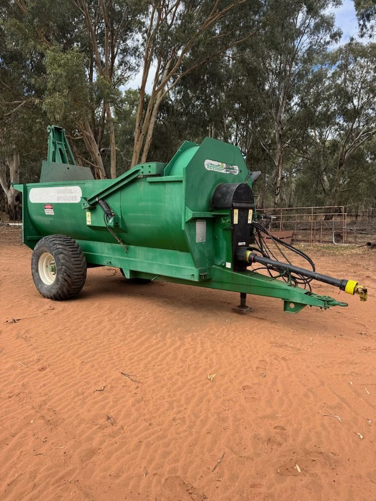 Green agricultural machine on sandy ground with trees in the background