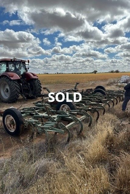 Farm machinery in a field under cloudy sky, with a cultivator marked “SOLD” in the foreground.