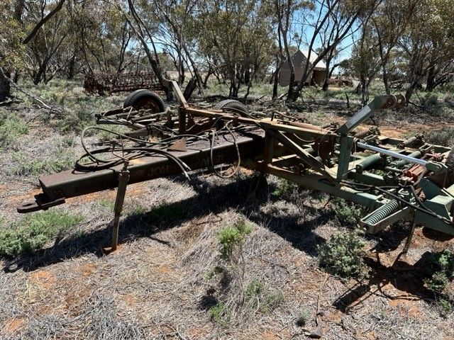 Rusty abandoned farm equipment in a dry, scrubby field with scattered trees