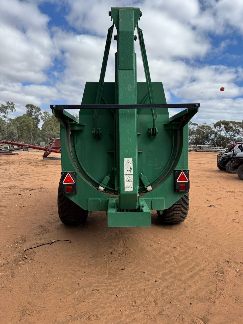 Rear view of a large green agricultural trailer on a dirt road under a cloudy sky