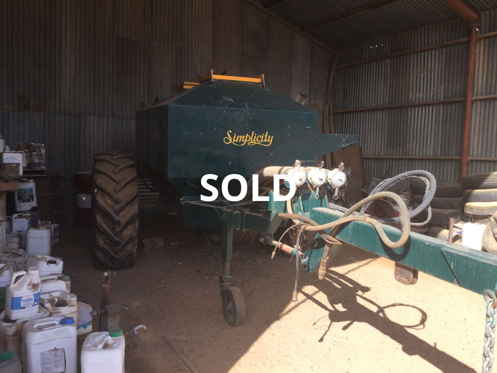 Green combine harvester in a shed with farming equipment and supplies; sold sign on the machine.