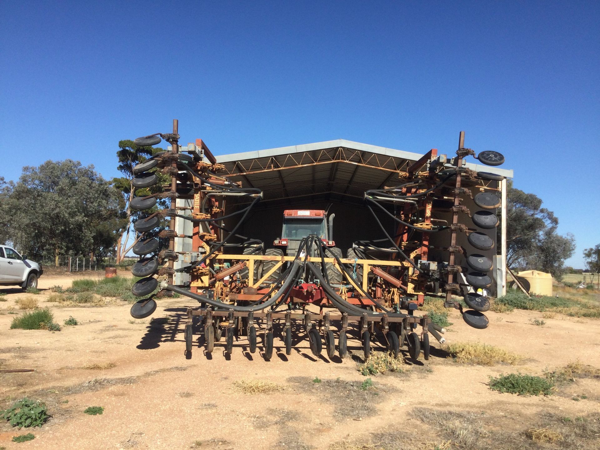 Front view of a large farm implement with multiple metal discs in a dry field under a blue sky