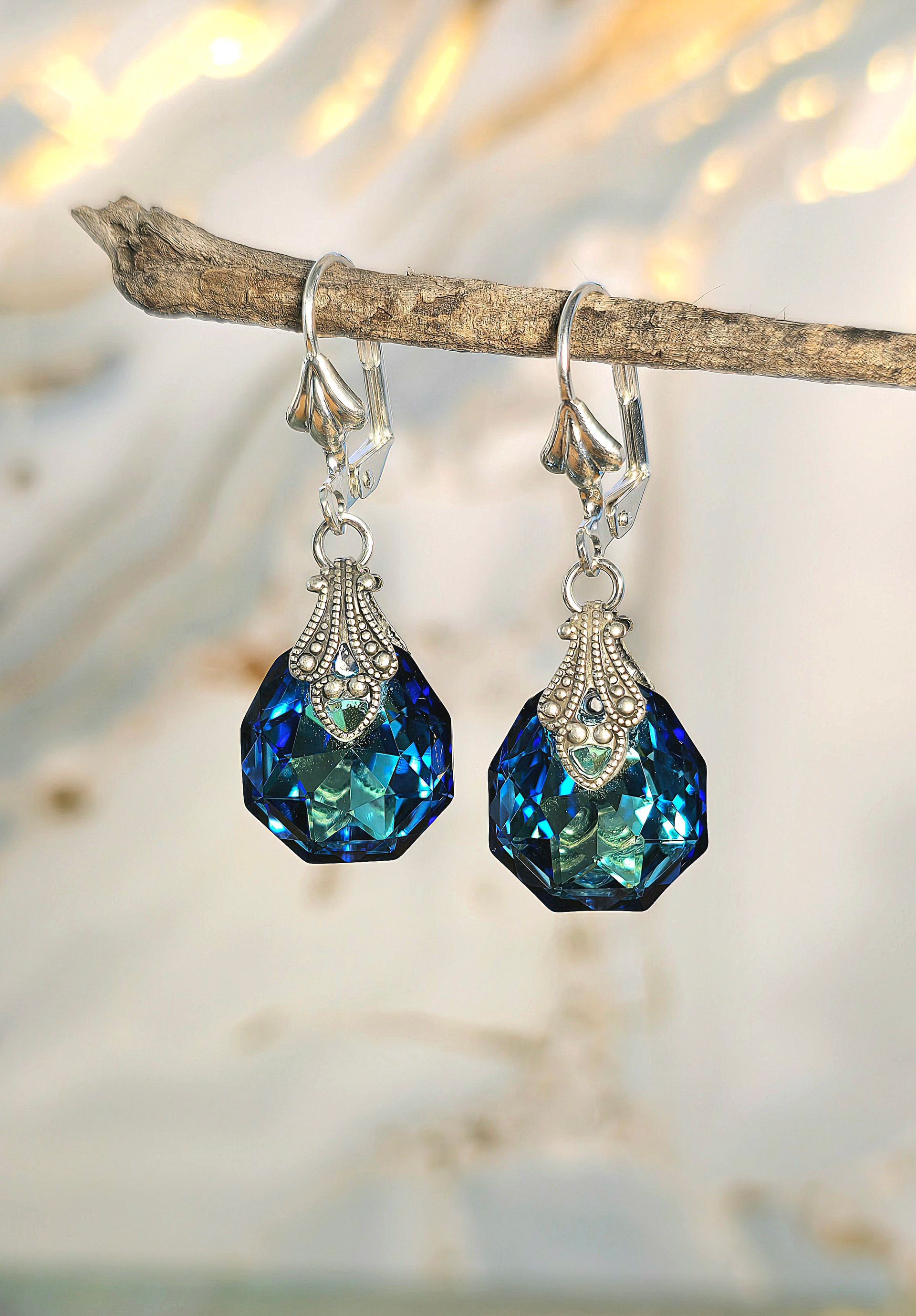 A pair of blue earrings are hanging on a branch.