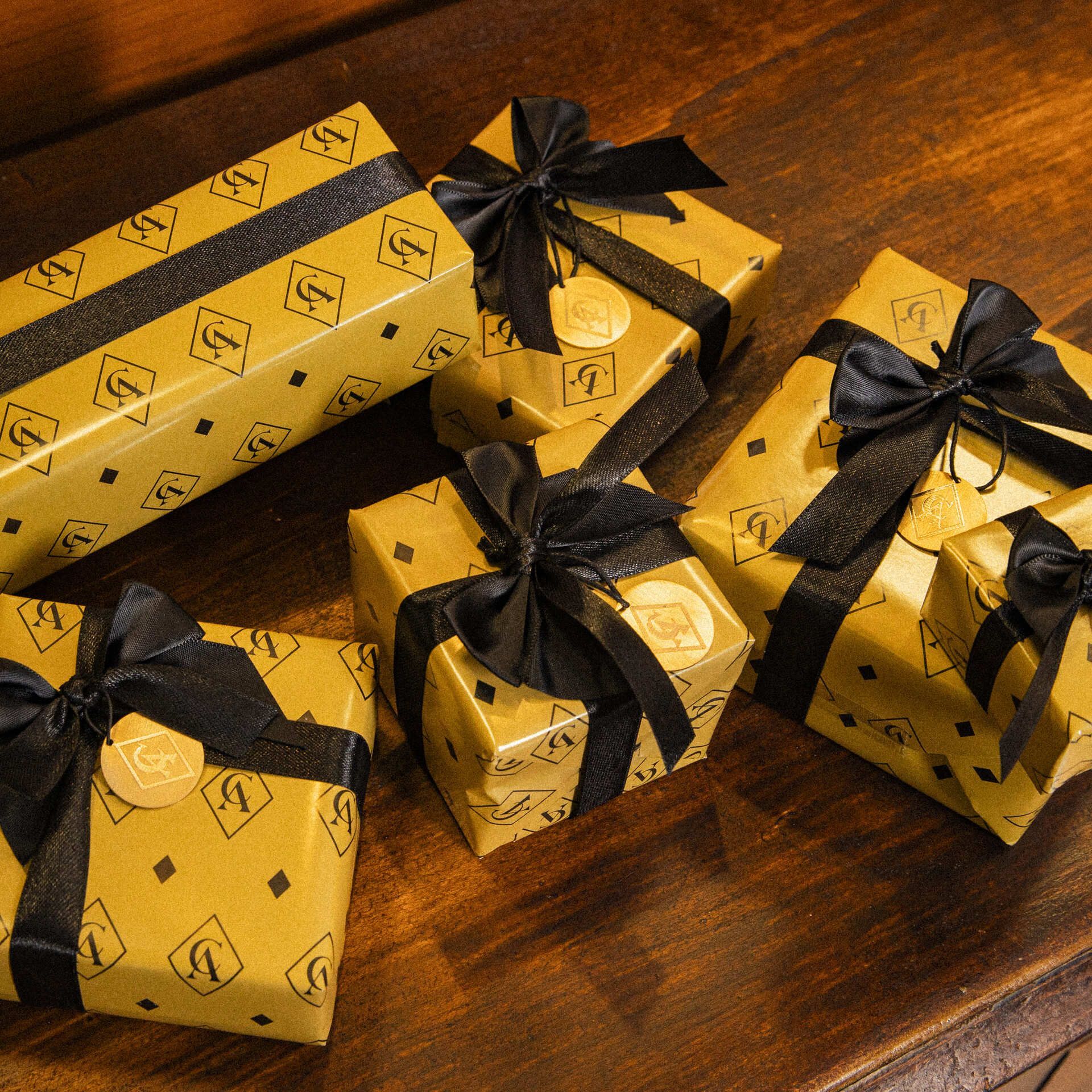 Confezioni regalo_ pacchetti regalo dorati decorati con un motivo geometrico e nastri neri, disposti su un tavolo di legno Confezioni regalo_ pacchetti regalo dorati decorati con un motivo geometrico e nastri neri, disposti su un tavolo di legno