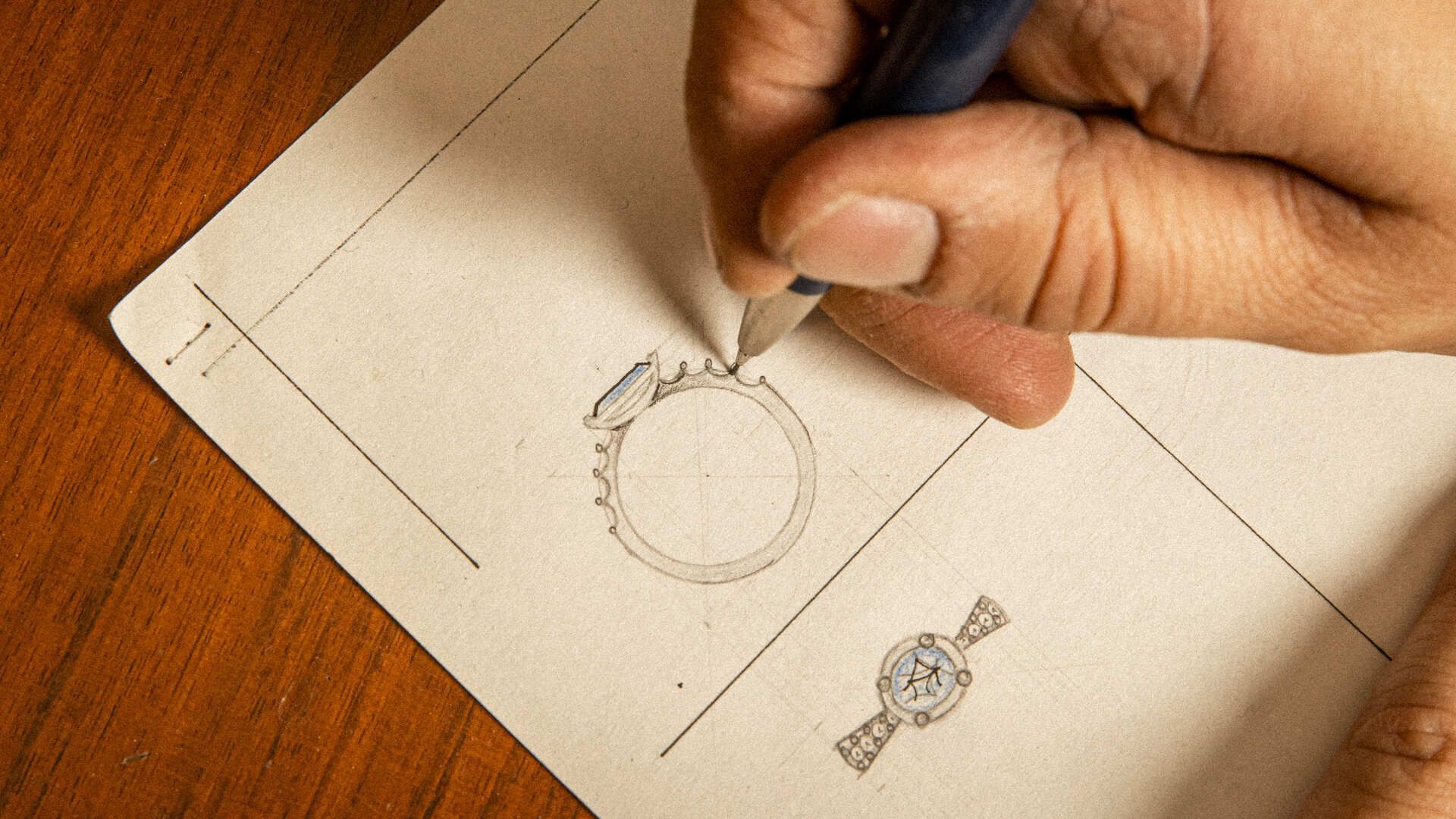 Disegno tecnico di gioielli: Mani che tracciano a matita il progetto di un anello su carta da disegno, con altri schizzi di gioielli visibili Disegno tecnico di gioielli: Mani che tracciano a matita il progetto di un anello su carta da disegno, con altri schizzi di gioielli visibili