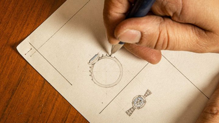Disegno tecnico di gioielli: Mani che tracciano a matita il progetto di un anello su carta da disegno, con altri schizzi di gioielli visibili