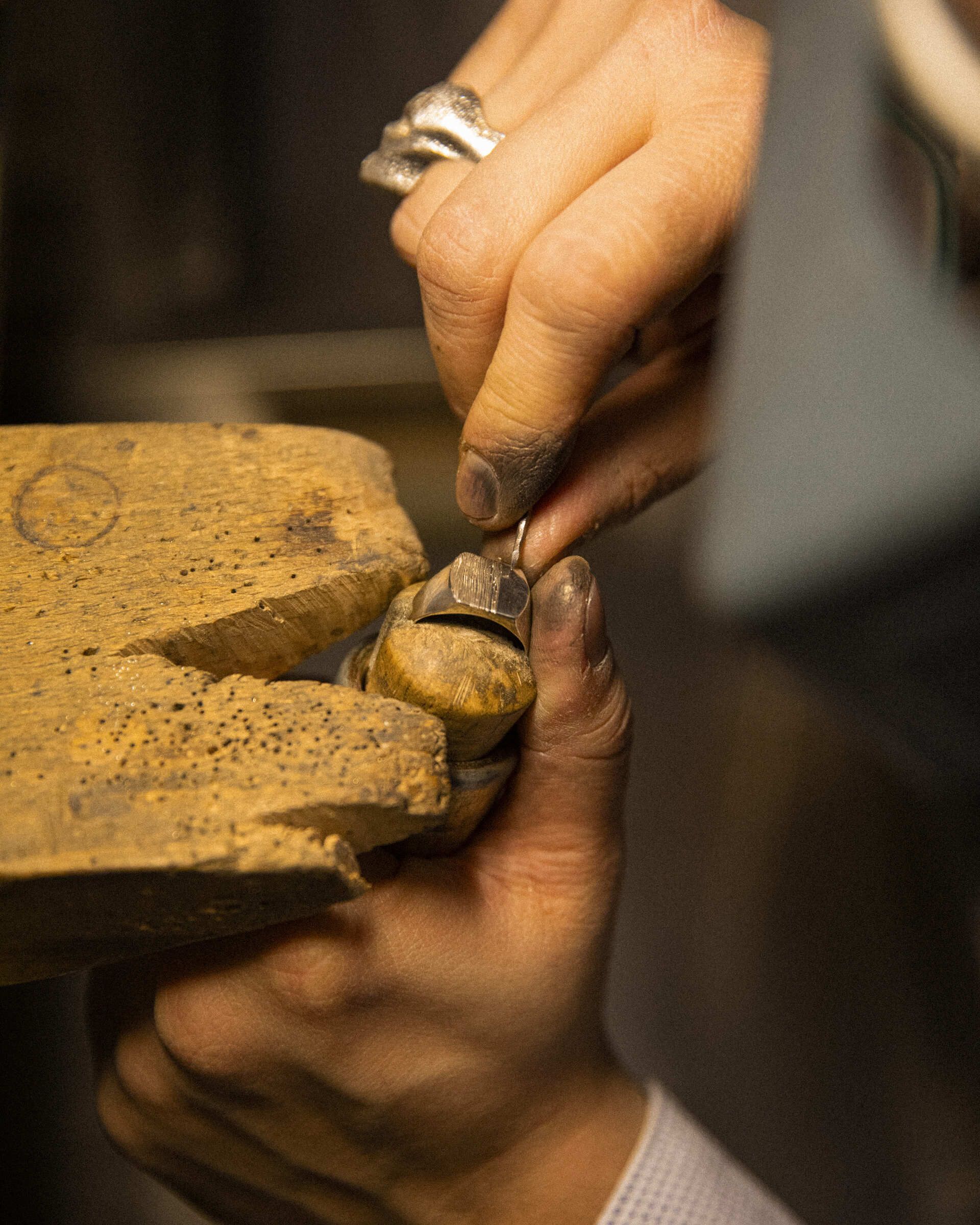 Mani di Andrea che usa uno strumento per incastonare una gemma su un gioiello, posizionato su un banco da lavoro Mani di Andrea che usa uno strumento per incastonare una gemma su un gioiello, posizionato su un banco da lavoro
