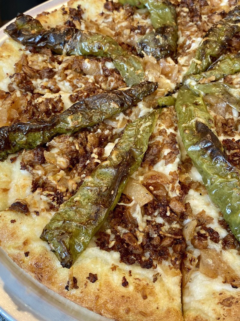 A pizza with green peppers and meat on it is on a pan.