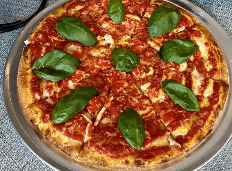 A pizza with tomato sauce and basil on a pan