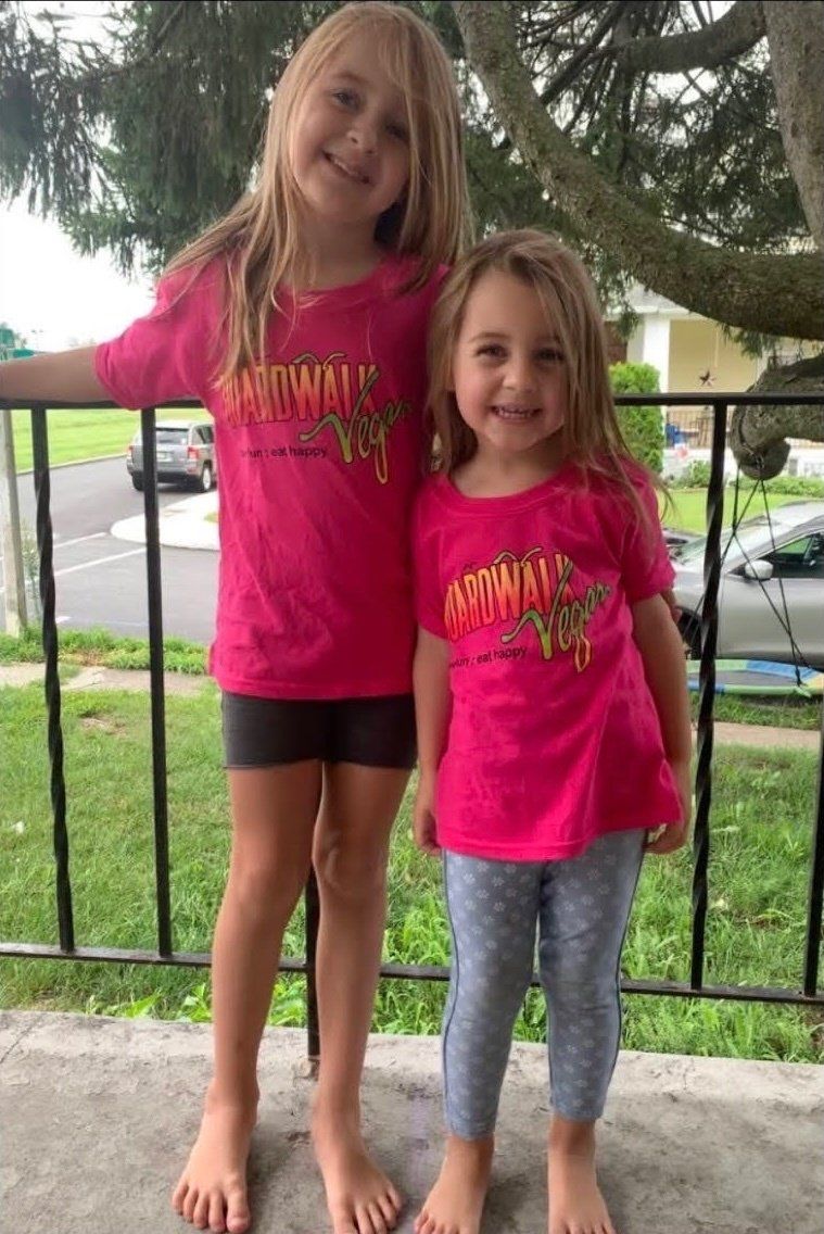 Two little girls wearing pink shirts are standing next to each other on a porch.