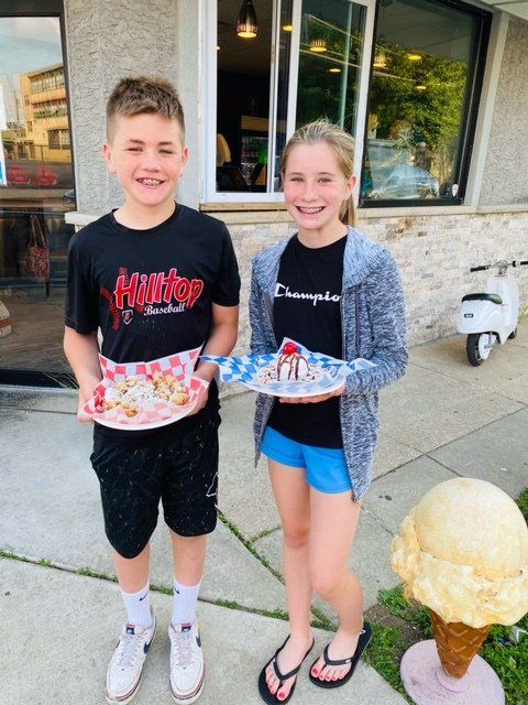 A boy and a girl holding plates of food in front of an ice cream cone