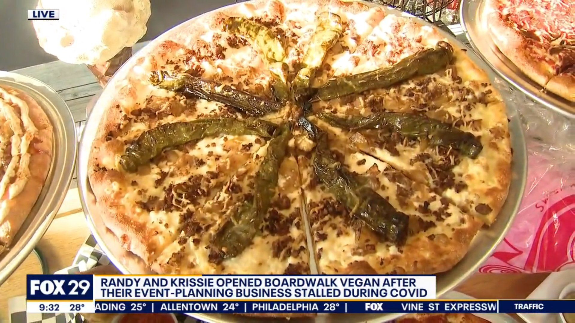 A pizza with pickles on it is sitting on a table next to other pizzas.