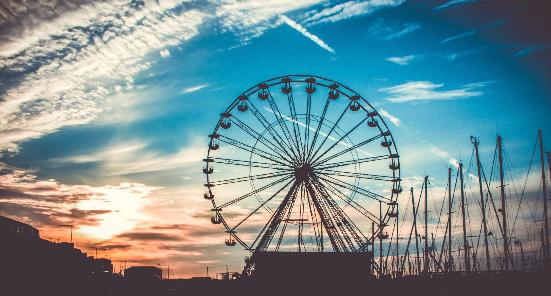 A ferris wheel is silhouetted against a cloudy sky at sunset.