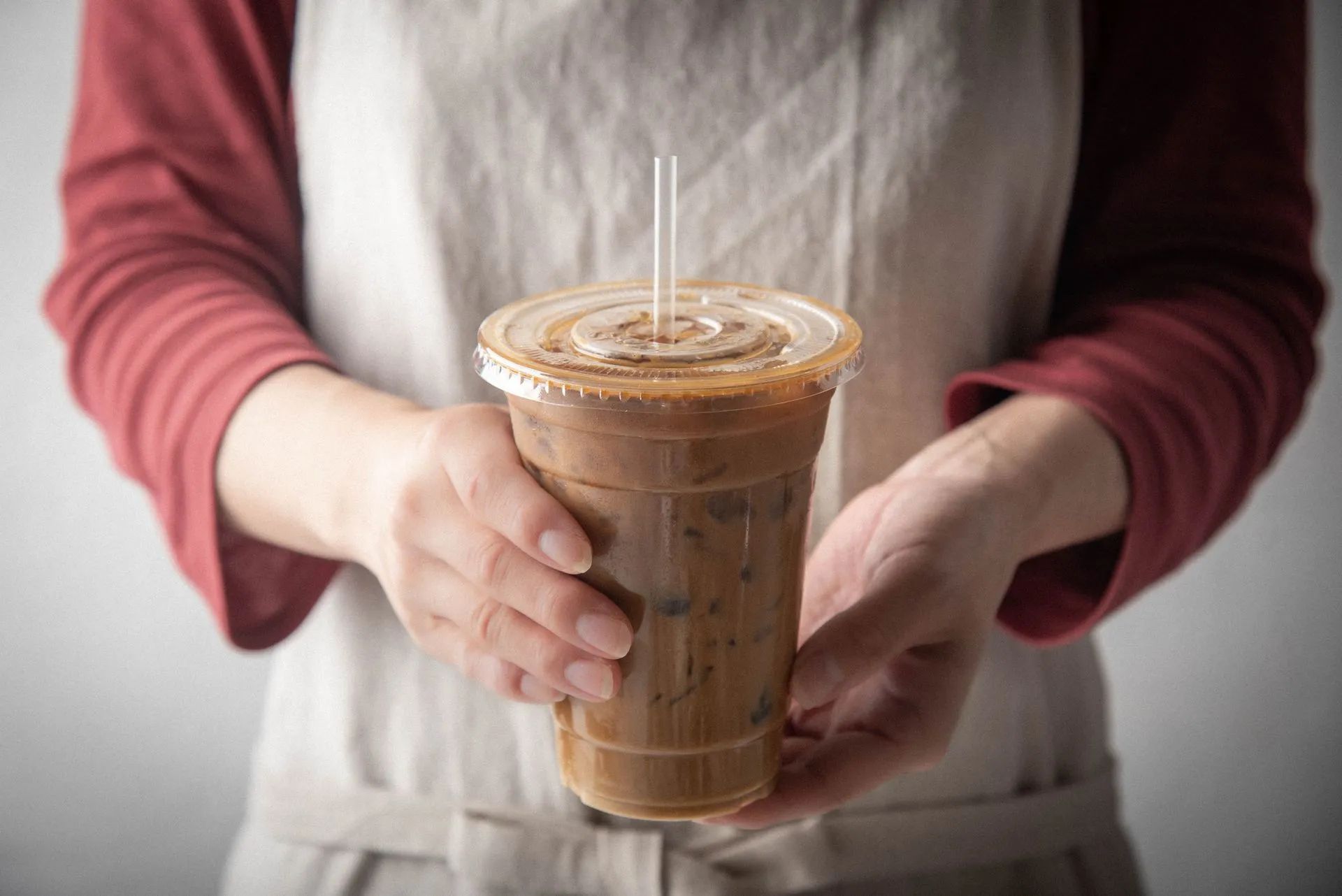 A woman is holding a cup of iced coffee with liquid sugar in it, one of many liquid sweeteners.