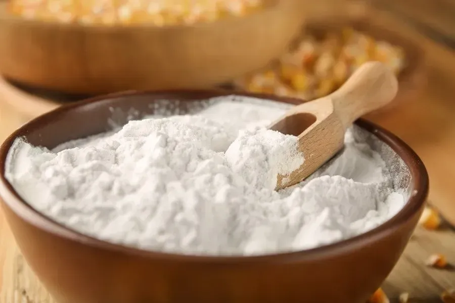 Bulk corn starch powder in a wooden bowl with a small wooden scoop.