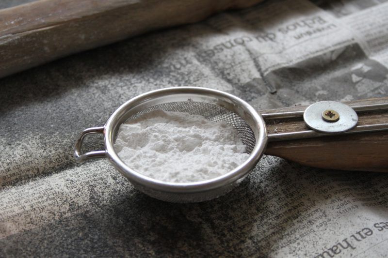A strainer filled with bulk powdered sugar on top of a newspaper.