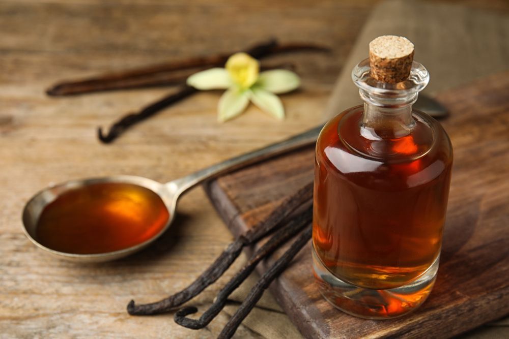 Bottle of vanilla syrup with vanilla beans and a spoon on a table, highlighting emulsion vs extract.