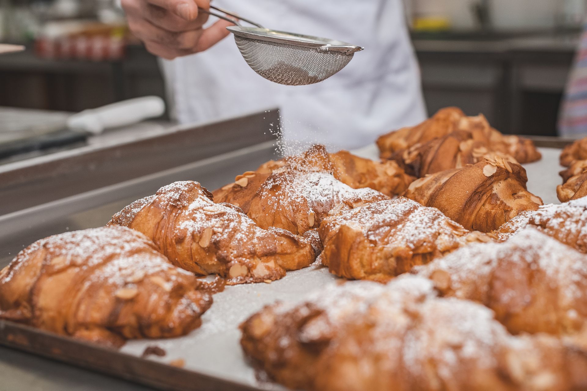 a baker sprinkles powdered sugar ontop of almond croissants