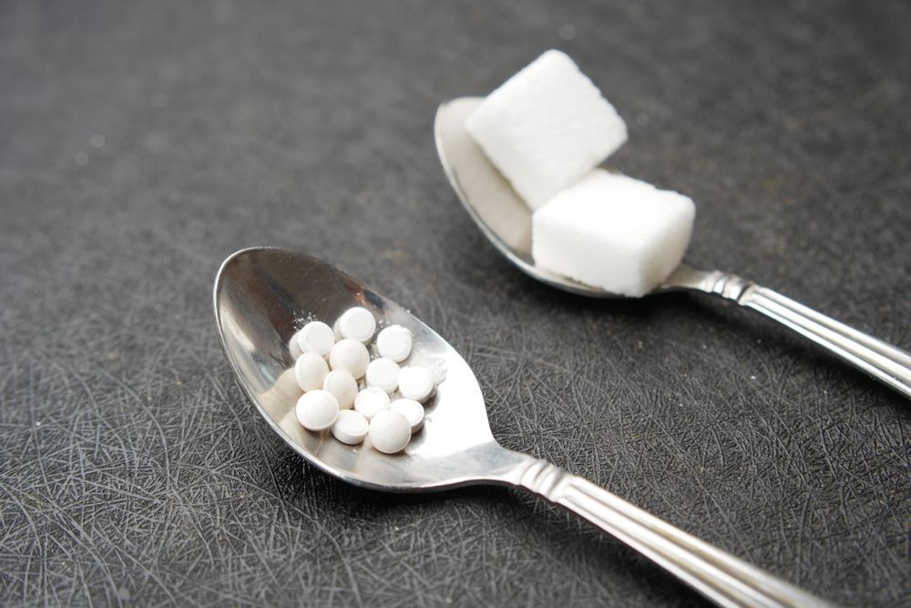 Two spoons filled with sugar cubes and artificial sweetener