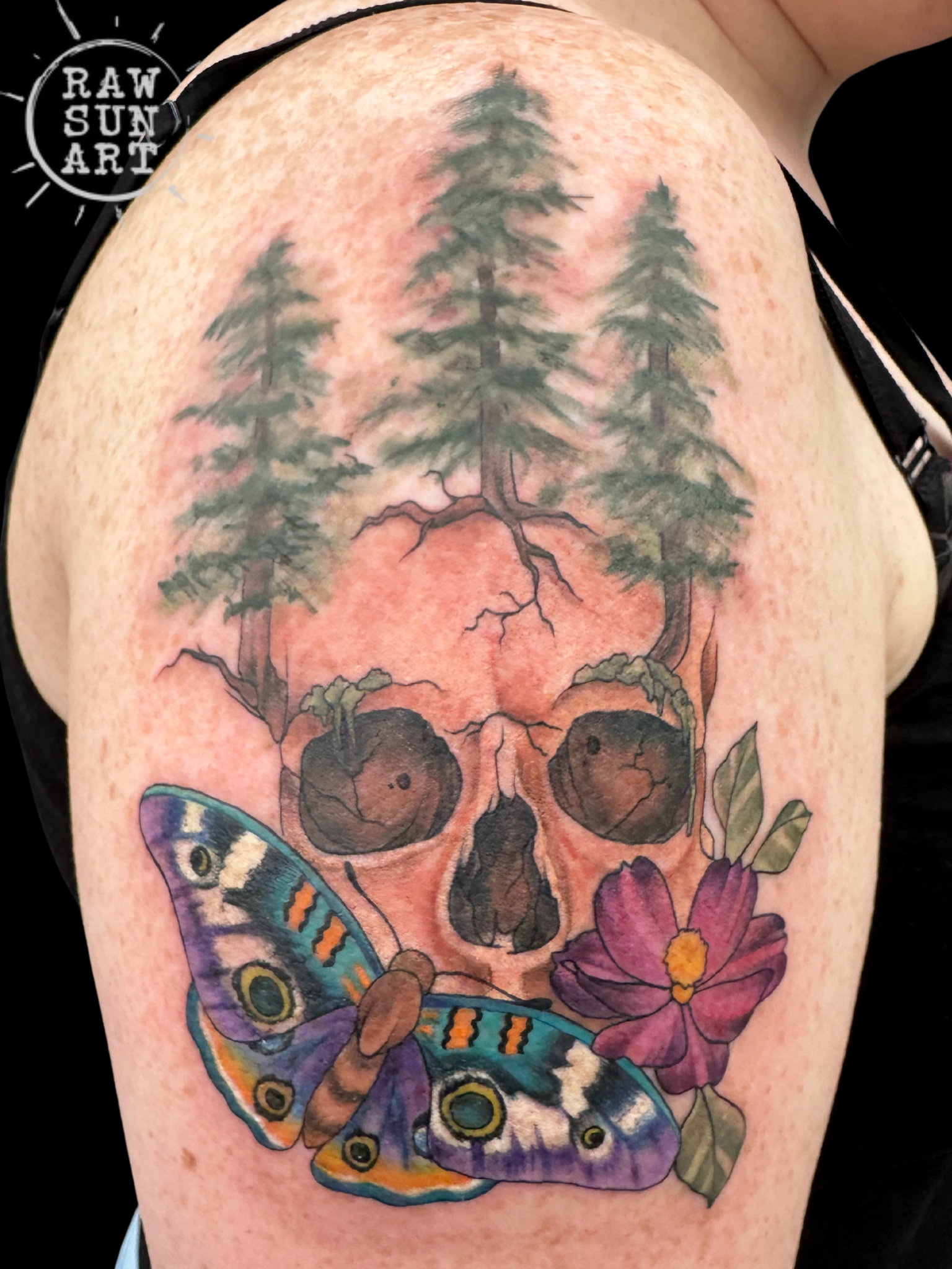 A tattoo of a skull with trees and flowers on it