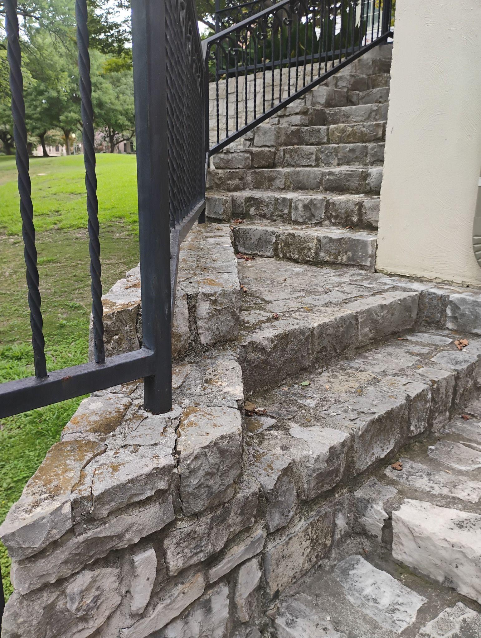 Stone staircase with uneven, cracked steps beside a black metal railing and white wall outdoors