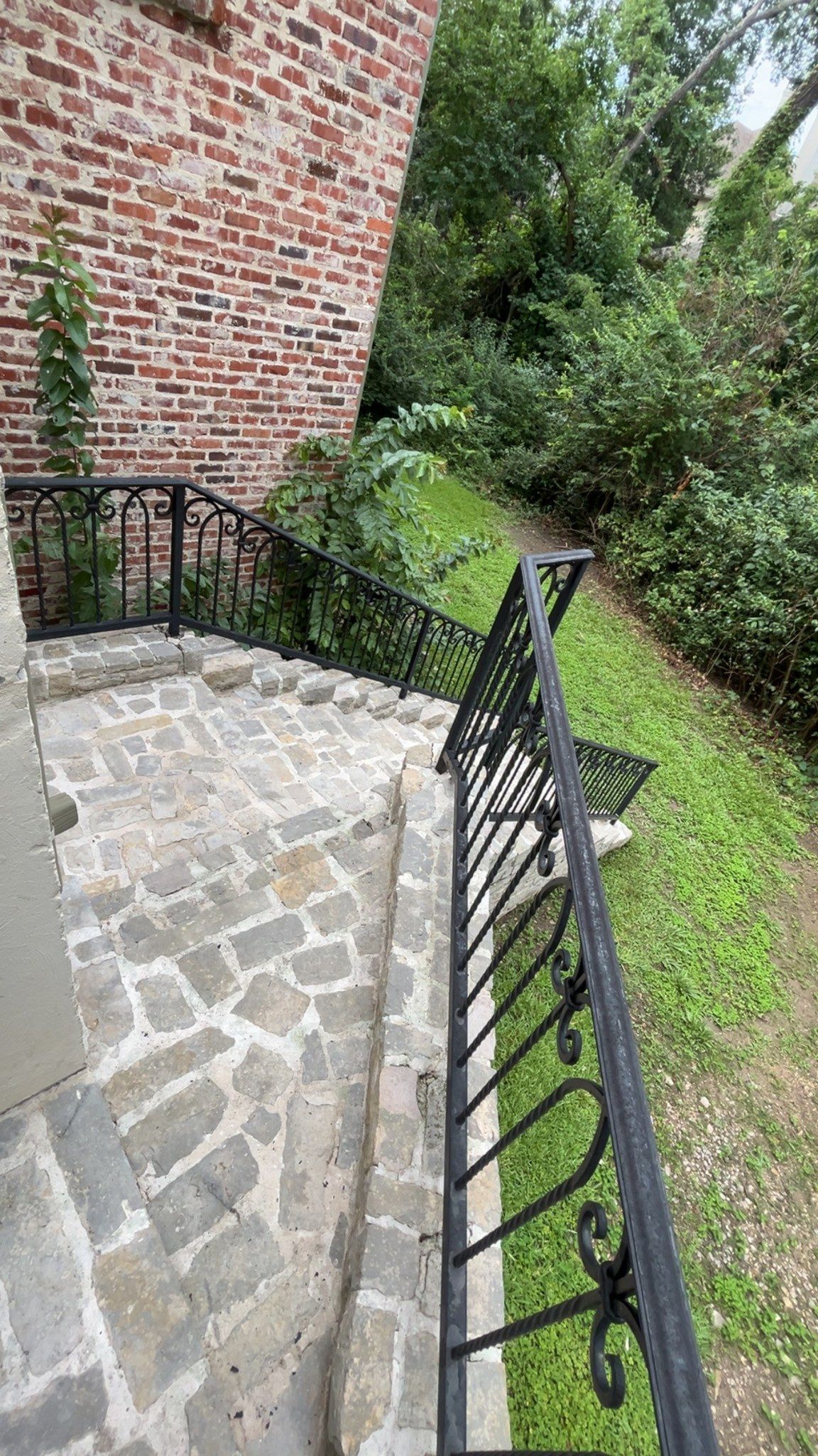 Stone patio with black metal railing beside a red brick wall and green garden path