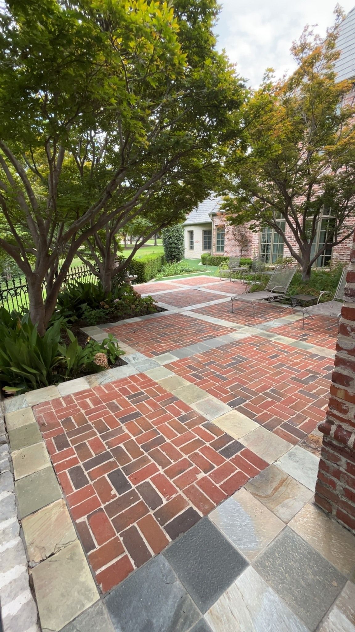 Brick and stone walkway leading through a leafy garden to a house entrance